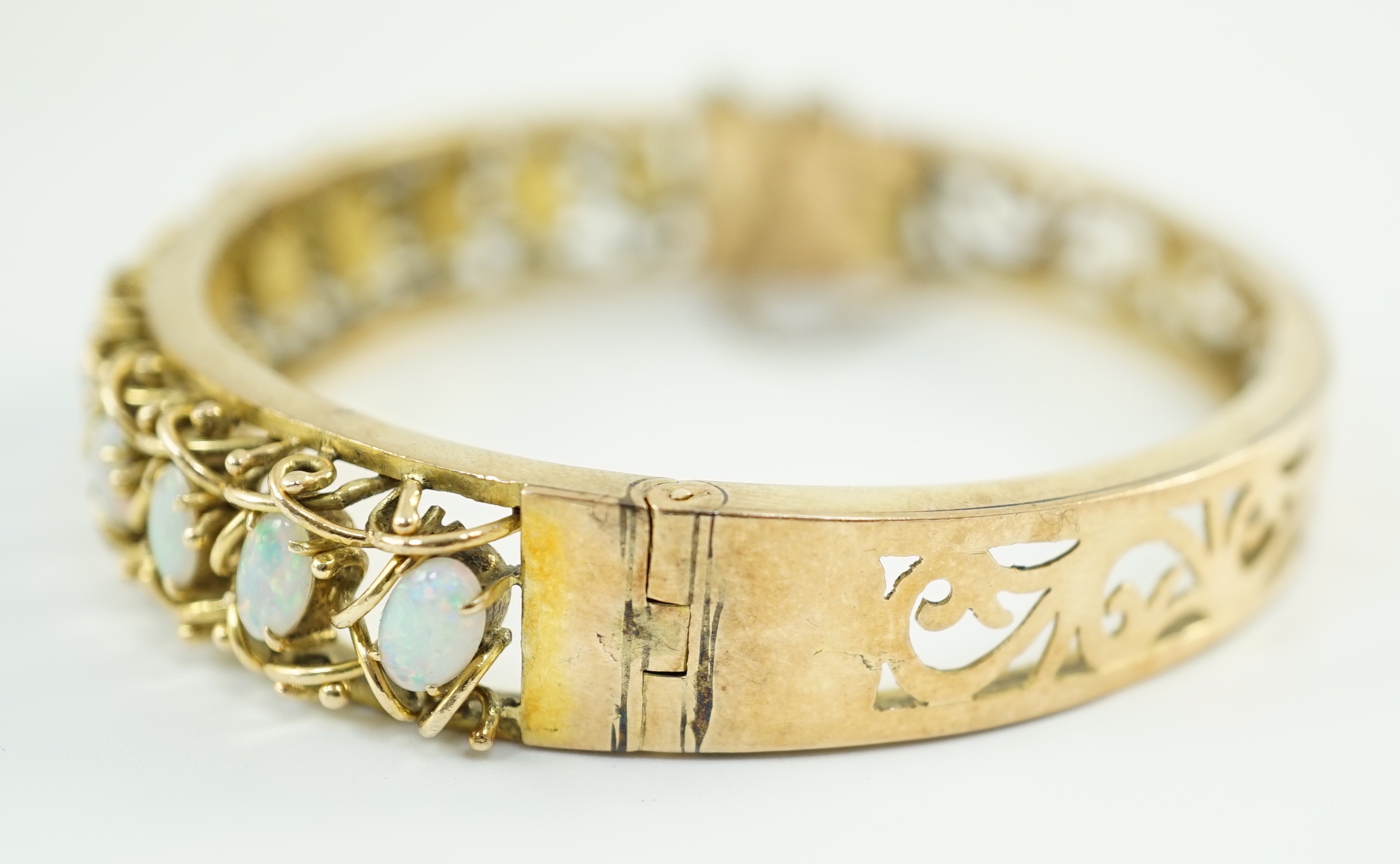 A pierced gold and twelve stone oval white opal set hinged bangle